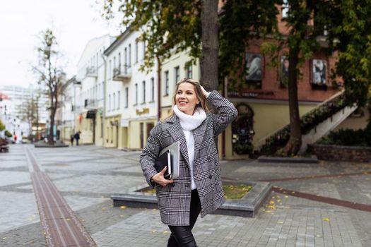 an adult woman lawyer with a smile on her face hurries to work with a laptop in her hands against the backdrop of a city panorama.