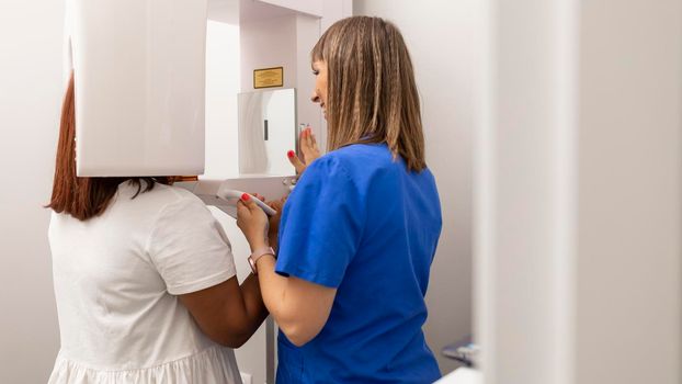 A dentist woman setting up the cbct scanner for one of their clients at the dental clinic