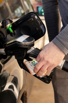 Car refuelling on petrol station. Man refilling car with fuel and holding money, euros. Close up. Gasoline, diesel is getting more expensive. Petrol industry and service. Petrol price and oil crisis