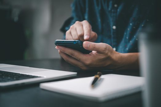 Man holding a phone with a pen and paper to write a note in an office diary using a laptop at office.