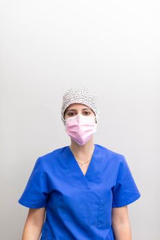 Portrait of a white dentist woman posing for the camera, wearing mask, medical hat and uniform after a day of work at the dental clinic