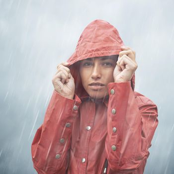 Gray skies. Cropped portrait of a young young woman pulling up her hood while standing in the rain