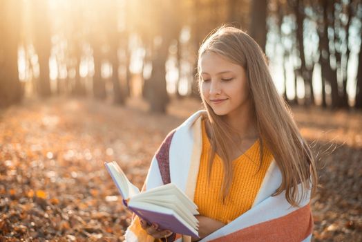 Bright warm photo of a girl with a book in autumn park covered with yellow foliage