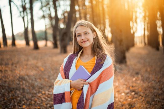 Cheerful girl having a walk in park full of vibrant autumn colours, reading a book, admiring beauty of nature