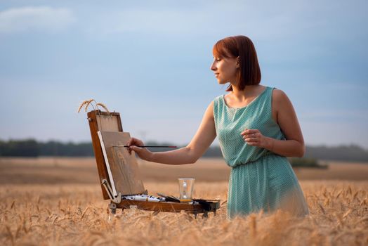 Girl painter working outdoors in the agricultural field of ripe grain