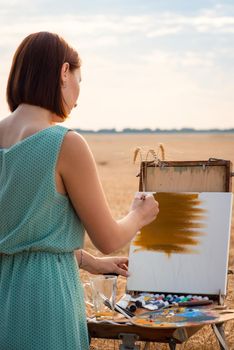 Beautiful girl doing her favourite hobby alone in the field, admiring the beauty of nature, making art