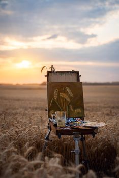 Artist drawing painting of rye ears in the big field with a setting sun in the background