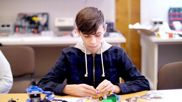 the boy of 12 years, plays in the designer from cubes, plates, circuits, wires. a small inventor creates robots, machines from different parts of the designer. High quality photo