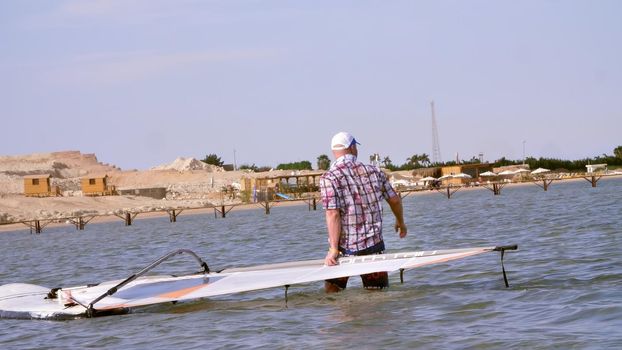 a man pulls the windsurfing board , man learns to ride on a board with a sail, windsurfing on the crystal clear water. High quality photo