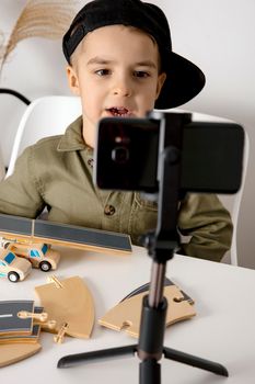 Adorable, cute, little boy blogger recording lifestyle blog, talking to camera of smartphone on tripod. Young influencer filming vlog for his channel. Child makes video for his followers online