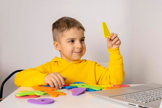 Adorable, cute, little boy learning alphabet online, with laptop at home. Child using e-learning platform to make video call with his teacher and study. Homeschooling and distance education for kids