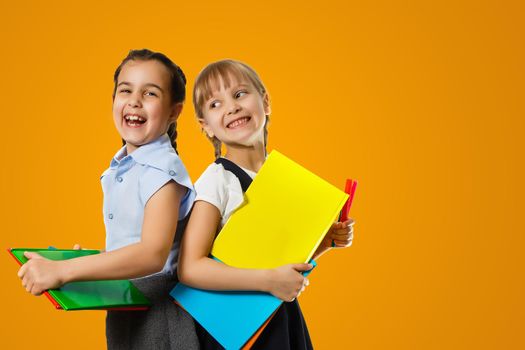 Education Concept. Set portrait of diverse schoolchildren holding stack of academic books and wearing backpack, yellow orange color studio background.