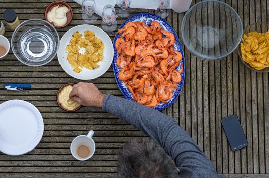Overhead view of man enjoying prawns and mayonnaise in an outdoor setting