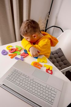 Little boy learning alphabet and numbers online, with laptop at home. Child is sad and tired. Negative emotions, stress, mental problems. Homeschooling and distance education for kids