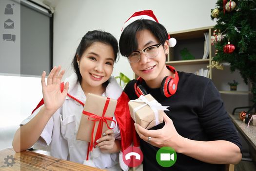 Happy couple holding Christmas gift and having video call.
