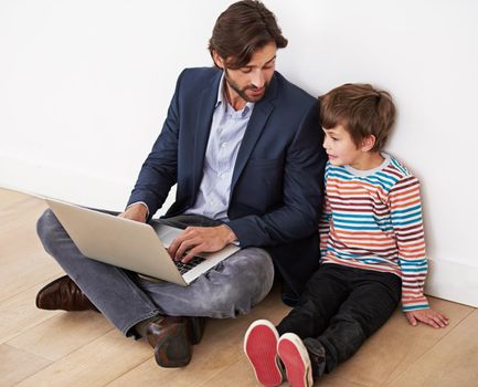 Technology brings them together. A father and son sitting on the floor with a laptop