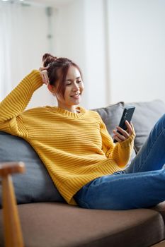 portrait of a young Asian woman woman holding smartphone while sitting on sofa.