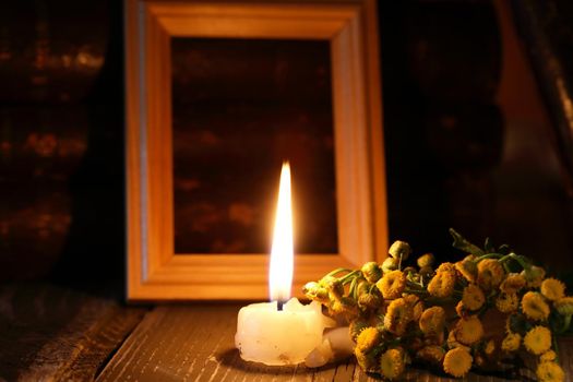 One lighting candle near bunch of wild flowers against free picture frame