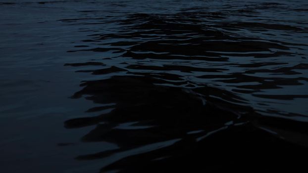 Sea surface at the night - dark background with neutral wave texture. Wallpaper with water close up.