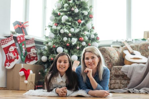 Mother with her child daughter celebrating near Christmas tree.