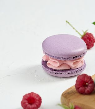 One purple macaroon and red raspberries on a white background	