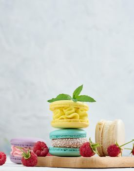 Stack of multicolored macaroons and red raspberries on a white background