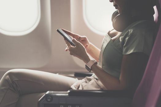 Joyful asian woman sits in the airplane and using mobile phone while go to travel.