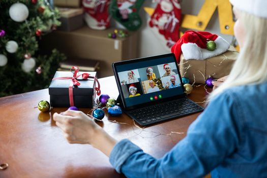 Woman with santa hat using video call conference on tablet, decorations and lights at home. Caucasian adult for christmas eve party.