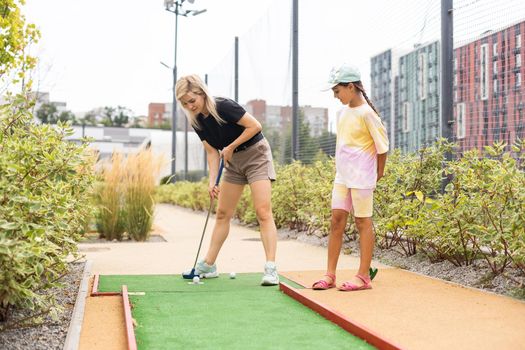 Detail of young woman and daughter playing mini adventure golf on a beautiful sunny summer day.