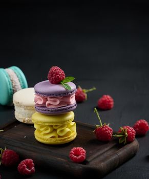 A stack of multi-colored macaroons on a wooden board. Delicious dessert