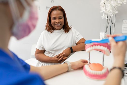 A black woman patient watches her dentist's explanation on how to correctly brush her teeth at the dental clinic