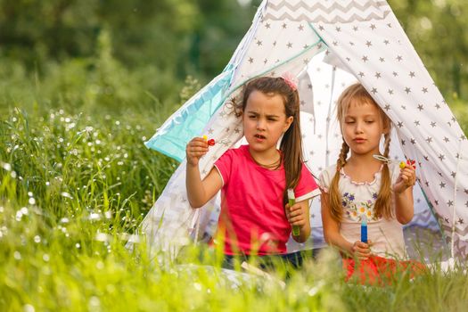 childhood and hygge concept - happy little girls playing in kids tent.