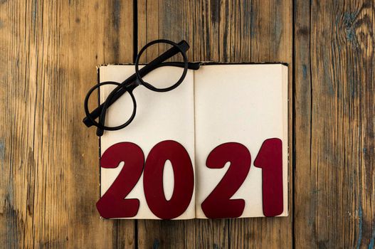 Copy space of number 2021 lay on open vintage book and eyeglasses on wood table background with text space. New year concept