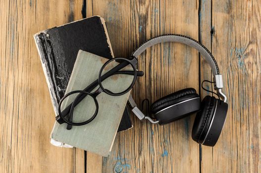 Closed old vintage books, black headphone and glasses on a wooden table. Top view