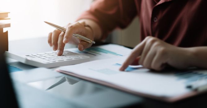 Young Business woman working on desk office with using a calculator to calculate the numbers, finance accounting concept. work from home concept.