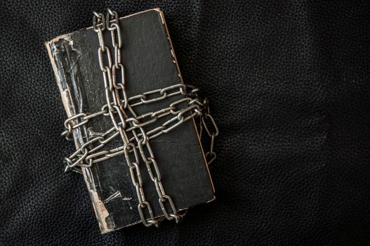 Old book bound by a new shiny chain on dark background.