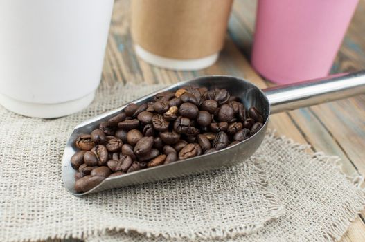 Disposable take-out mockup paper cups with coffee beans for morning espresso and spoon in brown bowl on wooden background