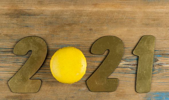 Top view of number 2021, symbol of the coming New Year, colorful macaroons on rustic wooden background. Conceptual Holiday background.