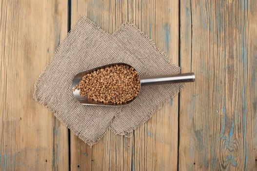 Raw, natural, uncooked buckwheat seed kernels in metal scoop on wooden table. Traditional food. 