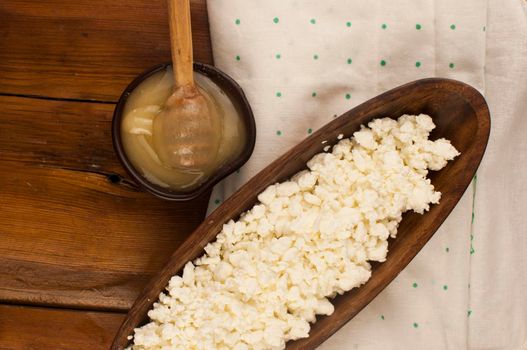 Cottage cheese with honey in a clay bowl on wooden background, top view