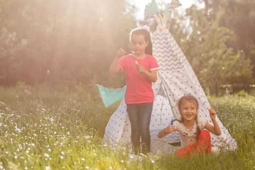 Two happy laughing little girls in camping tent in dandelion field.