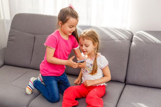 people, children, technology, friends and friendship concept - happy little girls sitting on sofa and taking selfie with smartphone at home