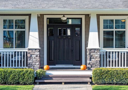 Decorative ripe pumpkins laying in front the house entrance, prepared for Helloween celebration.