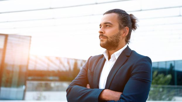 Successful businessman suit with beard standing in front of office glass building arm crossed confidently looking away. Hispanic male business person side view portrait. Web banner, Free space