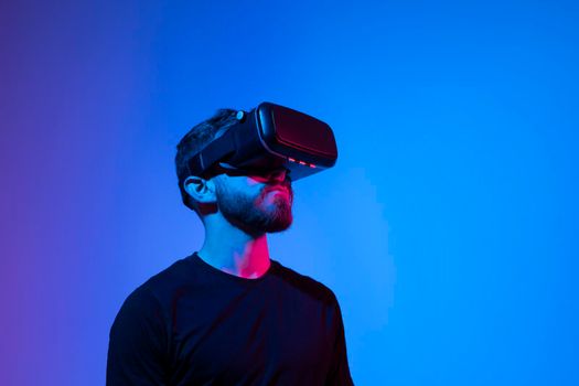 Man a gamer in black t-shirt in modern wireless glasses of virtual reality plays a video game in a dark room