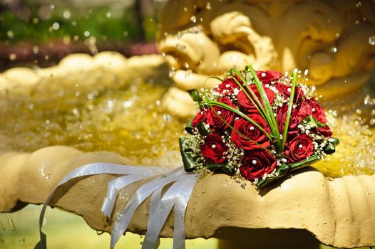 The Wedding Bouquet Of The Bride Of Red Roses Lies In An Old Fountain Under Splashes And Drops Of Water.. bridal bouquet of flowers in fountain water drops