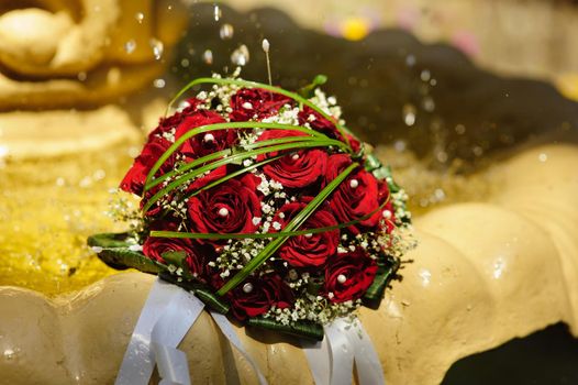 The Wedding Bouquet Of The Bride Of Red Roses Lies In An Old Fountain Under Splashes And Drops Of Water.. bridal bouquet of flowers in fountain water drops