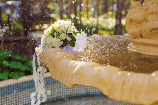 The Wedding Bouquet Of The Bride Of Red Roses Lies In An Old Fountain Under Splashes And Drops Of Water.. bridal bouquet of flowers in fountain water drops