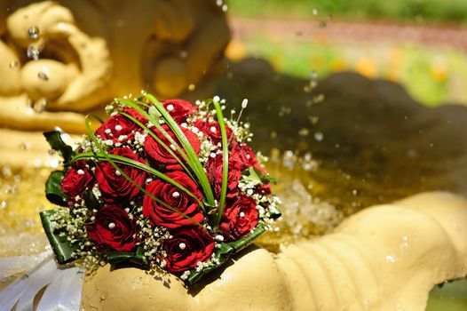 The Wedding Bouquet Of The Bride Of Red Roses Lies In An Old Fountain Under Splashes And Drops Of Water.. bridal bouquet of flowers in fountain water drops