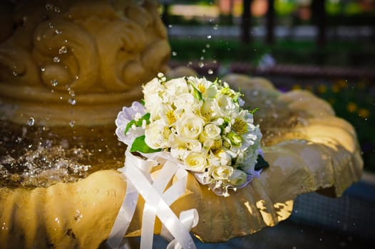 The Wedding Bouquet Of The Bride Of Red Roses Lies In An Old Fountain Under Splashes And Drops Of Water.. bridal bouquet of flowers in fountain water drops